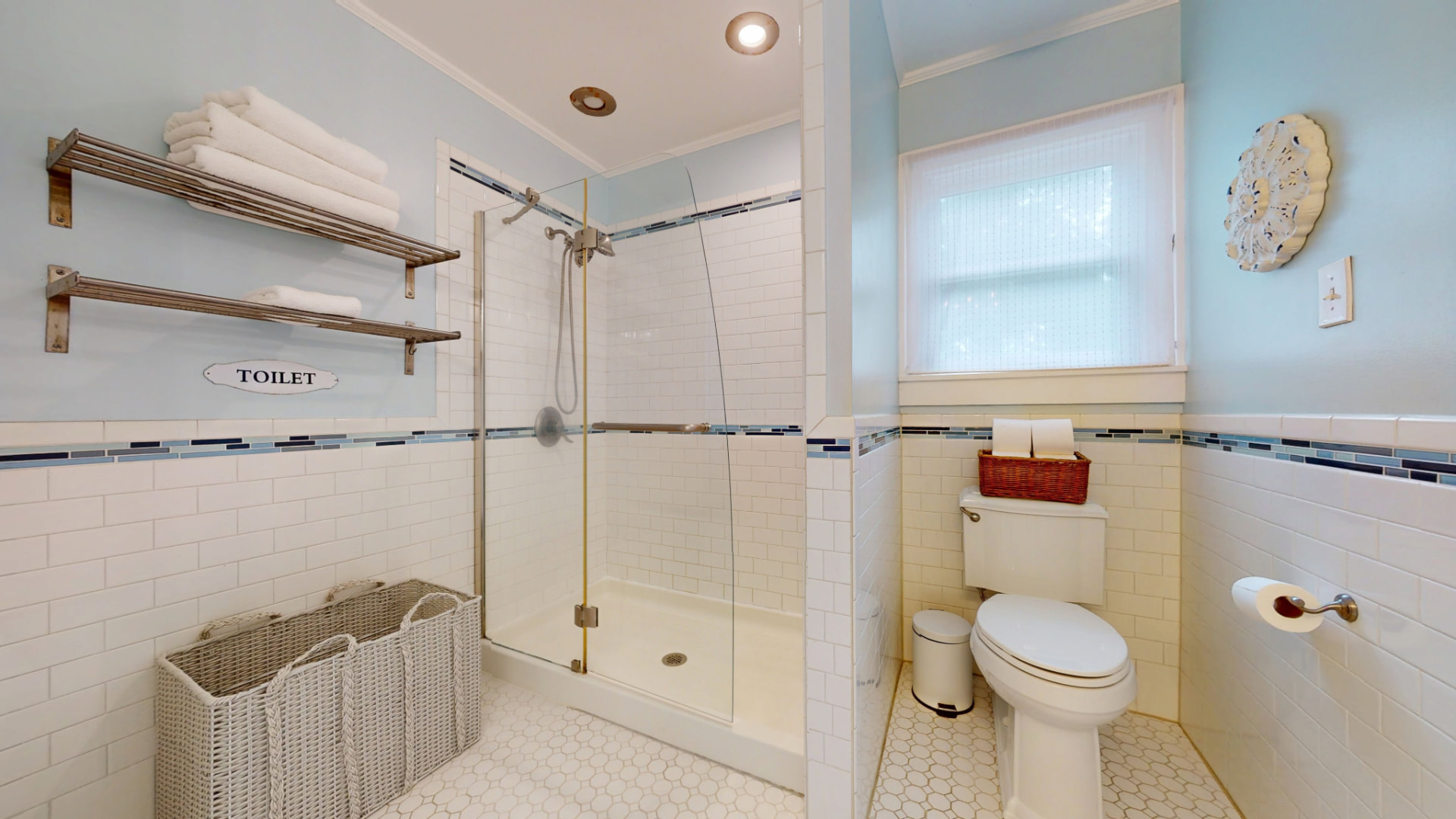 Second bath with walk-in glass shower, white subway tile, blue mosaic accent stripe, and open towel shelving
