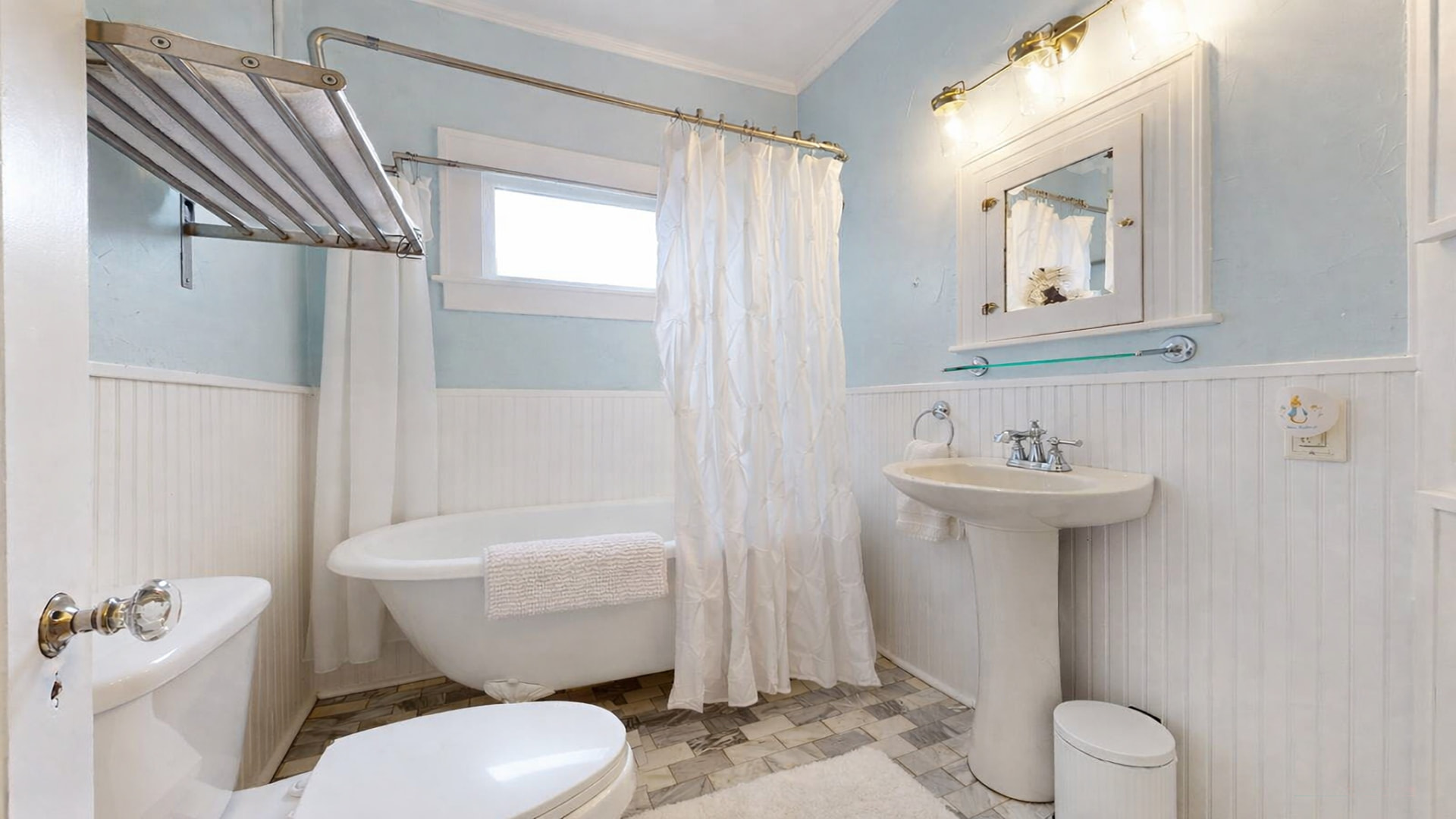 Full bath with clawfoot soaking tub, beadboard wainscoting, pedestal sink, and marble herringbone floor