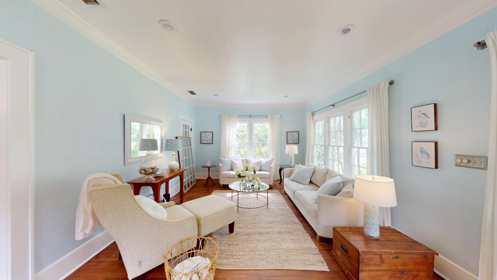Living room with pale blue walls, crown molding, hardwood floors, and tall windows facing the front garden